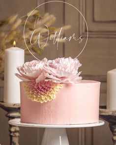 a pink cake sitting on top of a table next to two white candles and flowers