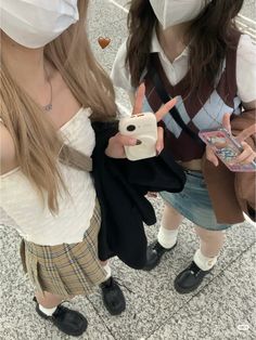 two girls wearing face masks and holding cell phones in their hands while standing next to each other