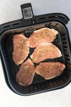 four pieces of raw chicken in a black air fryer basket on a white surface