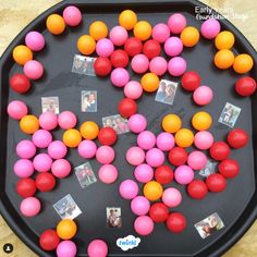 a tray filled with pink and orange balls on top of a wooden table next to pictures