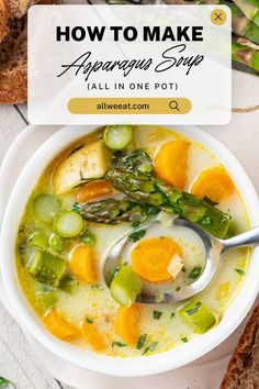 a bowl of soup with asparagus, carrots and bread on the side