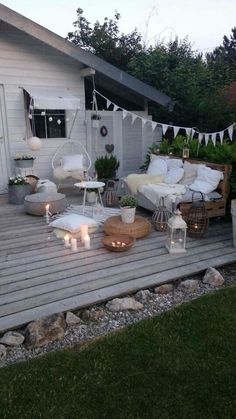 a deck with chairs, tables and candles in the middle of it is lit up by string lights