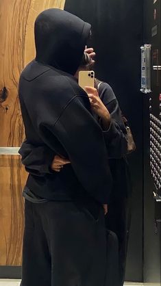 a man wearing a hoodie taking a selfie in front of a mirror with his cell phone