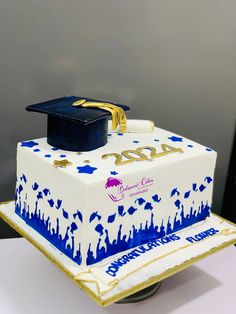 a graduation cake with blue and white icing on it's side, topped with a cap