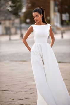 a woman in a white dress is standing on the street with her hands on her hips