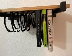 several books are sitting on a shelf with cords attached to the book ends, and one has a pair of scissors in it