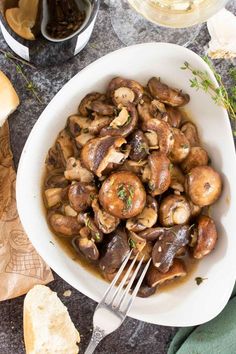 a white bowl filled with mushrooms on top of a table next to bread and wine