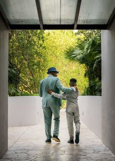 two men in suits and hats are walking through an open doorway with trees behind them