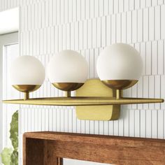 three white balls are mounted on a brass fixture in a room with striped wallpaper