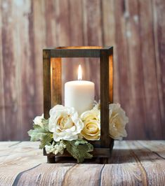 a white candle is sitting in a small wooden box with flowers on the inside and behind it