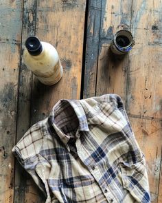 an old flannel shirt is sitting on a wooden table next to two empty bottles