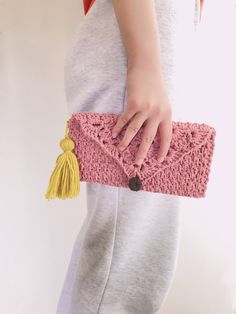 a woman is holding a pink crocheted purse with tassels on it