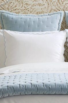 a bed with blue and white pillows on it's headboard in front of a floral wallpaper