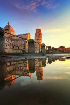 the leaning tower is reflected in the still water