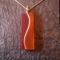 an orange and red piece of wood hanging from a necklace on a brown leather surface