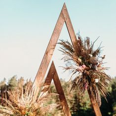 two tall wooden poles with flowers on them in front of some trees and grass at an outdoor wedding venue