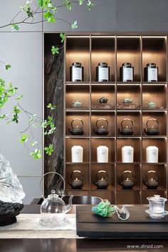 a table with some tea pots and cups on it next to a shelf filled with plants