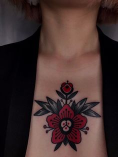 a woman's chest with a red and black flower tattoo on her left side