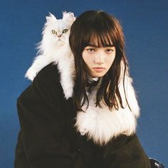 a woman holding a white cat on her shoulders in front of a blue background,