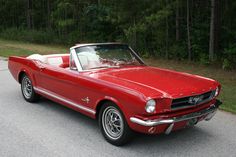 an old red mustang convertible parked on the side of the road in front of some trees