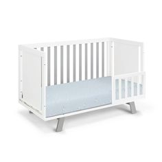 a white crib with a blue sheet on the bottom and side rails, in front of a white background