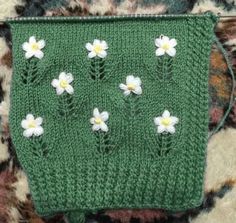 a crocheted purse with white flowers on the front and green handle, sitting on a carpet