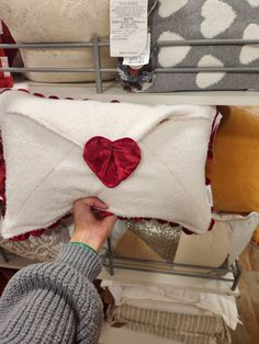 a woman is holding up a pillow with a heart on it in front of other pillows