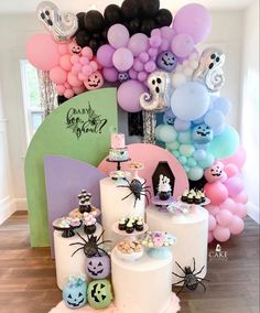 a table topped with lots of cakes and balloons in front of a wall filled with halloween decorations