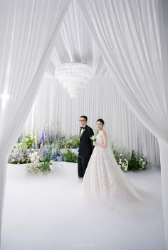 a bride and groom standing in front of white drapes