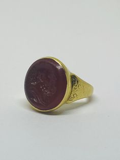 "This is a vintage 18K (high-karat) yellow gold Cameo-design statement ring. Definition of a \"cameo\": a piece of jewelry, typically oval in shape, consisting of a portrait in profile carved in relief on a background of a different color. Material(s): 18K yellow gold + unidentified material (cameo) Total weight: 12.2 grams Flaws (if any): None to mention Marking(s): \"18ct\" (translating to 18K gold) Measurements: The face of the ring measures 17.9 millimeters in height by 5.8 millimeters in wi Formal Gold Cabochon Signet Ring, Classic Yellow Gold Signet Ring With Cabochon, Gold Heirloom Signet Ring With Cabochon, Heirloom Gold Signet Ring With Cabochon, Formal Yellow Gold Ruby Ring With Cabochon, Classic Gold Ruby Ring With Cabochon, Classic Gold Ruby Cabochon Ring, Gift Yellow Gold Cabochon Signet Ring, Victorian Yellow Gold Cabochon Jewelry