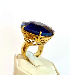 A beautifully hand crafted ring showcases a 100 carats round-cut blue natural Sapphire with hearts design motifs. The ring has been made in 92.5 silver with 18k yellow gold-plated, and has a layer of nickel underneath the gold-plating. Only 1 is available. Clarity - Opaque Type     - Natural Sapphire Colour - Blue Sapphire size: 27.6 mm Length x 27.6 mm Width x 14 Depth mm, 100 carats Total ring size: 28.65 mm Length x 28.65 mm Width x 15 mm Depth of ring sit on the finger 92.5 sterling silver 1 Sapphire Colour, Gold Drop Necklace, Sapphire Cocktail Ring, Design Motifs, Green Emerald Ring, Blue Origin, Hearts Design, Unusual Rings, Sapphire Color