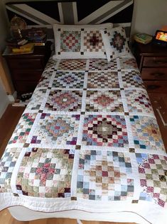 a bed with a quilt on top of it next to a night stand and dresser