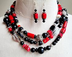 Make a statement and wear this stone necklace with several outfits in your wardrobe or give it as a gift. Strung with assorted cut and polished black onyx stones, dyed red coral stones, silver and stainless-steel beads all combined in this chunky and elegant design.  This bib cluster necklace is strung on three wires and finished with a lobster clasp closure. The necklace has an inner diameter of 18 inches long, while the exterior diameter is 22 inches long. Matching assorted stone earrings are Red And Black Necklace, Chunky Stone Necklace, Red Coral Stone, Necklace Chunky, Black Onyx Stone, Coral Stone, Necklace Red, Cluster Necklace, Coral Jewelry