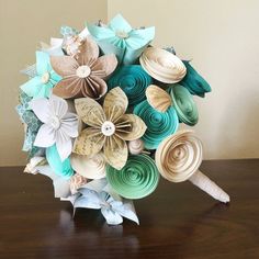 a bridal bouquet made out of paper flowers on a wooden table with a wall in the background