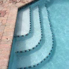 an empty swimming pool with steps leading to the water and brick pavers around it