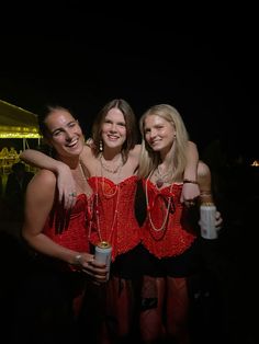 three women in red dresses standing next to each other at a night club with drinks