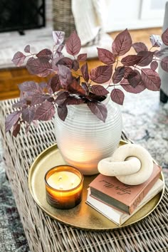 a table topped with a vase filled with purple leaves and a candle on top of a plate