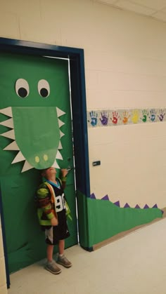 a young boy standing in front of a green door with a paper alligator on it