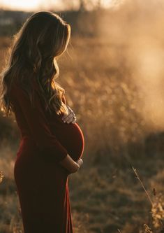 a pregnant woman in a red dress standing in a field