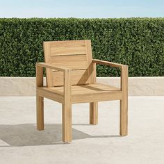 a wooden chair sitting on top of a cement floor next to a green hedge covered wall