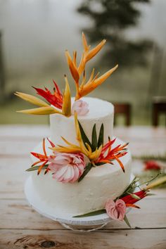 a white wedding cake with flowers on the top and bottom is sitting on a wooden table