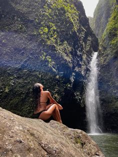 a woman sitting on top of a rock next to a waterfall