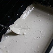 a spatula is being used to mix batter into an oven pan with white icing