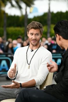 a man sitting in a chair talking to another man who is holding his hand out