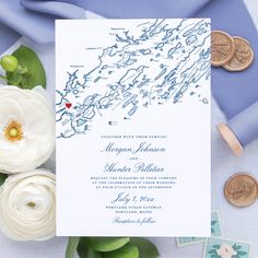 a white and blue wedding card on top of a table next to some flowers, coins and other items