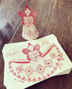 two christmas cards on a wooden table with paper cut outs in the shape of angels and snowflakes