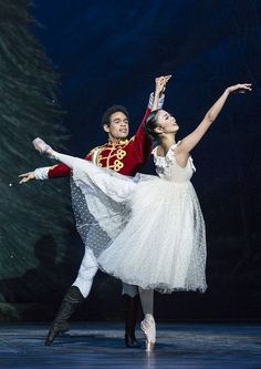 two ballerinas in white tutus and red jacket, one is holding the other's leg