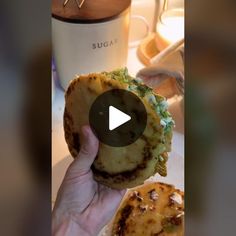 a person holding up a sandwich with cheese and lettuce on it in front of a coffee cup