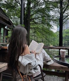 a woman sitting on a bench reading a book in the park with her back turned to the camera