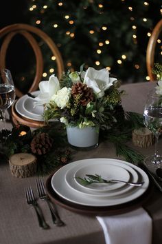 a table set for christmas dinner with white flowers and greenery on the place setting